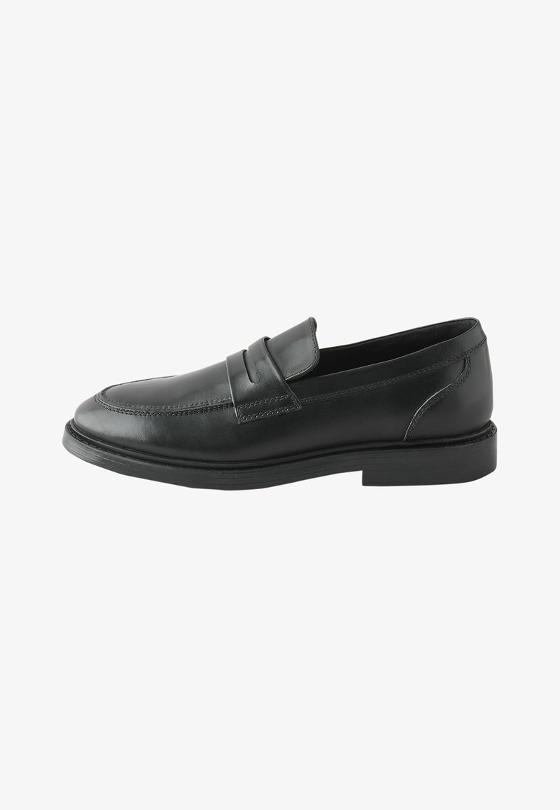 Mocassin homme en cuir noir avec un petit talon, une couture moc toe et une bride sur le dessus, présenté en profil.