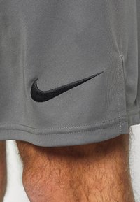 Šedé sportovní šortky vyrobené z texturované látky, s černým vyšitým logem Nike poblíž lemu a bočním rozparkem pro lepší pohyb.