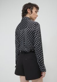Schwarze und weiße Bluse mit Punkten, einem Kragen und geknöpften Manschetten, kombiniert mit eleganten schwarzen Shorts mit Gesäßtaschen.