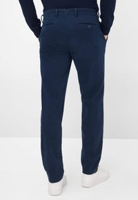 Pantaloni blu navy, design a gamba dritta, realizzati in un tessuto liscio. Presentano due tasche posteriori con bottoni e una vita sicura.