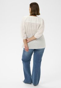 Witte, gestructureerde blouse met driekwartmouwen, met een achterpand en plooien, gecombineerd met uitlopende blauwe denim jeans.