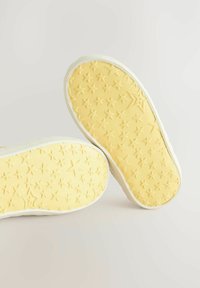 Semelles de chaussures en caoutchouc jaunes avec un motif texturé d'étoiles, présentant un bord blanc. Les semelles sont montrées sous un angle incliné sur un fond clair.