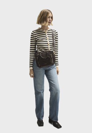 Braune Leder-Umhängetasche mit goldenen Beschlägen, Reißverschlusstaschen und strukturiertem Design. Das Modell trägt einen gestreiften Pullover und lockere Jeans.