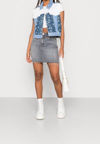 Jeansowa kamizelka w kwiatowy wzór, biały bawełniany krótki top, szara jeansowa spódnica oraz białe buty na sznurowadła. Prosty fason z postrzępionymi krawędziami.