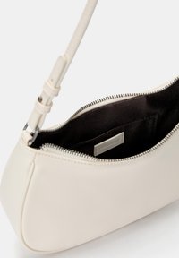 Cream faux leather bag with a smooth texture, zip closure, and a short strap; interior features a black lining with a brand label.