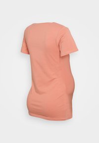 Camisa de manga curta na cor pêssego, feita de algodão suave, com decote redondo e silhueta ajustada, apresentando uma barra ligeiramente curva.