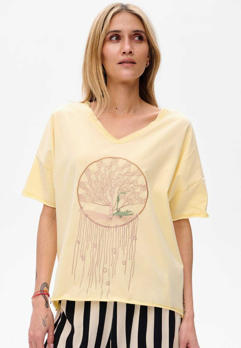 Geel V-hals T-shirt met een rond geborduurd ontwerp van een boom en intrigerende patronen. Korte mouwen, relaxte pasvorm, zachte textuur.