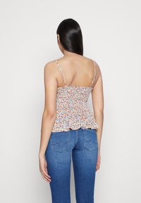 Top peplum floreale con arricciatura elastica, caratterizzato da piccoli fiori multicolori su uno sfondo chiaro. Spalline sottili e orlo arricciato.
