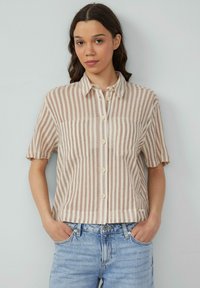 Korte mouwen, knoopsluiting overhemd in beige en crèmekleurige strepen, met een kraag, twee voorzakken en een ontspannen pasvorm. Draagt het met lichtblauwe jeans.