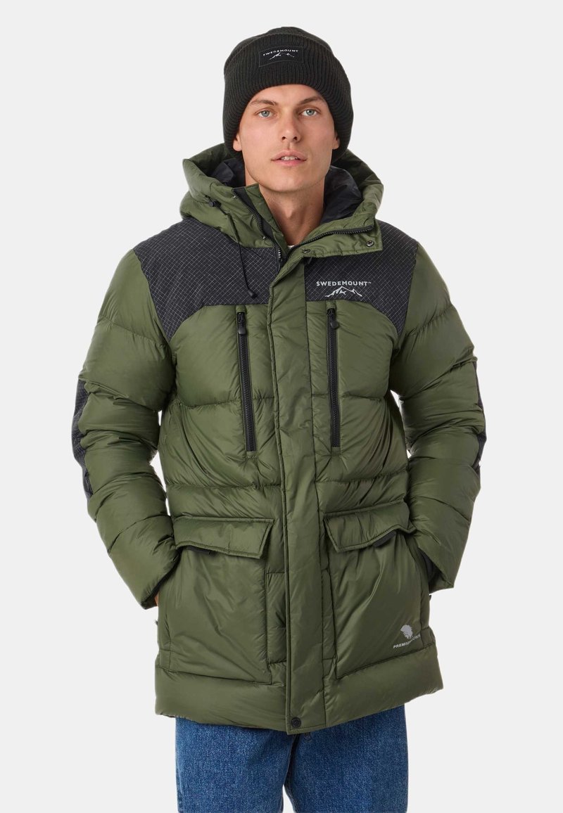 Green puffer jacket with a quilted black shoulder design, zippered pockets, and a hood. Paired with a black knit beanie.