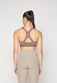 Brūns sporta krūšturis ar rasebra dizainu un krusteniski savilktām siksnām; saskaņots ar augsto jostasvietu beigu legingiem, kuriem ir ribota tekstūra.