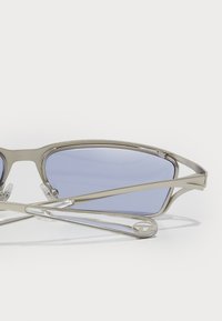 Akiniai nuo saulės su elegantišku metaliniu rėmu, mėlynomis tonuotomis lęšiais ir skaidriais akcentais. Išskirtinis geometrinis dizainas su sudėtingais šventyklomis.