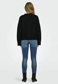 Maglione nero a maglia con una vestibilità comoda, abbinato a jeans skinny blu e stivaletti neri. Il maglione ha maniche lunghe e un collo tondo.