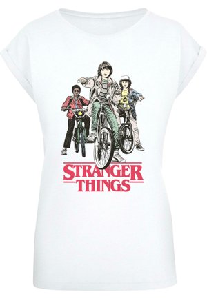 T-shirt en coton blanc avec un imprimé graphique de trois personnages à v�élo, avec le texte "STRANGER THINGS" en rouge vif en dessous.