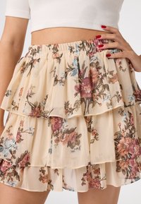 Jupe crème à motifs floraux avec trois volants superposés, taille élastique et illustrations détaillées de fleurs roses, bleues et marron.