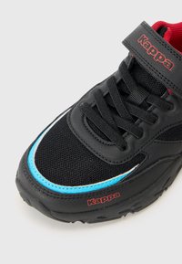 Svart sneaker med netting og syntetiske materialer, med en blå aksentlinje, rødt logo og svarte lisser med borrelåsrem.