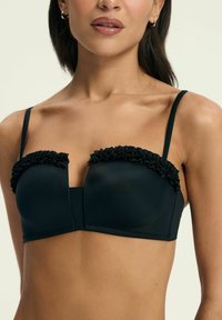 Czarny stanik z falbaniastymi akcentami wzdłuż górnej krawędzi, cienkimi regulowanymi ramiączkami oraz gładką fakturą materiału. Klasyczny wzór bielizny.