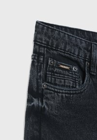 Jeans in denim scuro con una trama texturizzata, cuciture a contrasto, accessori in metallo e un piccolo logo applicato sulla tasca.