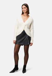 Cream fluffy cardigan with a deep V-neck, tied front, paired with a black faux leather mini skirt, sheer black tights, and pointed flats.