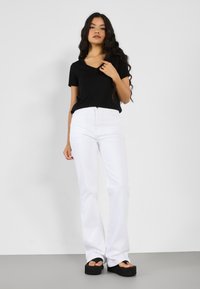 Crna v-neck majica u kombinaciji s bijelim trapeznim trapericama i crnim platformskim sandalama. Outfit ima ležeran dizajn s pripijenim siluetom.
