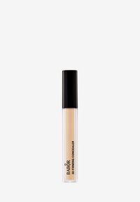Transparente Tube mit Concealer und schwarzem Deckel, der eine beige Flüssigkeit enthält. Markenlogo auf der Seite des Tubus sichtbar.