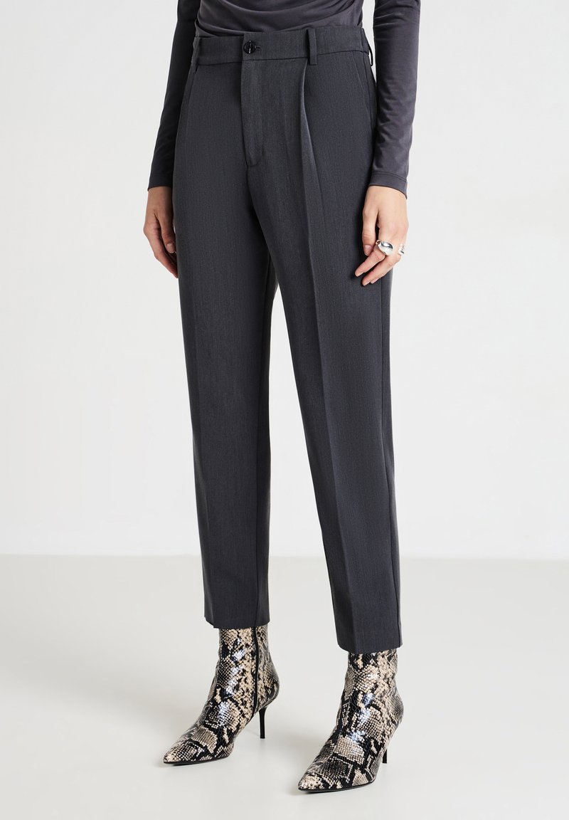 Pantalons en gris, bien coupés, avec une jambe droite et des plis, associés à des bottines à talons aiguilles en imprimé serpent, à bout pointu.