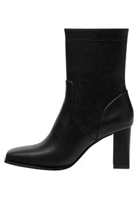 Bottine noire en cuir synthétique lisse avec un bout pointu et un talon bloc côtelé. Présente des coutures minimales et des découpes sur les côtés.