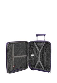 Maleta rígida morada con un mango retráctil. Por dentro presenta un forro negro con patrones geométricos y correas elásticas cruzadas para asegurar los objetos.