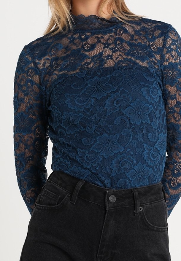 Top a maniche lunghe in pizzo blu navy con motivi floreali, trasparente e con colletto alto, abbinato a jeans in denim neri a vita alta.