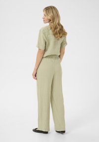 Ensemble en lin vert clair composé de deux pièces, comprenant un crop top à manches courtes et un pantalon taille haute ample. Chaussures plates noires.