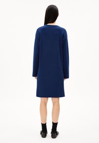 Robe tricotée surdimensionnée bleu marine avec manches longues, col rond et silhouette droite, tombant mi-mollet, réalisée en tissu doux.