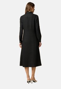 Schwarzes Leinenhemdkleid mit langen Ärmeln, Kragen und geknöpften Manschetten, gerade geschnitten und knielang.