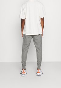 Ljust beige t-shirt med avslappnad passform i kombination med gråa sweatpants. Vita och oranga sneakers. Fokus på bekväm, avslappnad sportklädsel.