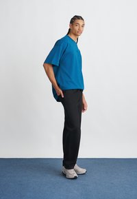 Τυρκουάζ oversized T-shirt με κοντά μανίκια, συνδυασμένο με μαύρο παντελόνι και γκρι αθλητικά παπούτσια. Λείος υφασμάτινος χαρακτήρας; απλός, χωρίς στολίδια σχεδιασμός.