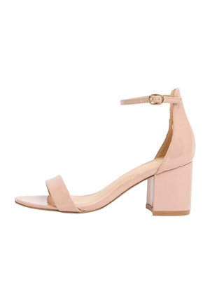 Beige Sandale aus lackiertem Leder mit offenem Zehenbereich, dickem Blockabsatz und Knöchelriemen mit goldener Schnalle vor weißem Hintergrund.