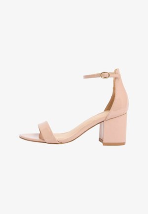 Sandale cu toc gros și deschis în față, din piele lacuită bej, cu baretă la gleznă și cataramă aurie pe fundal alb.