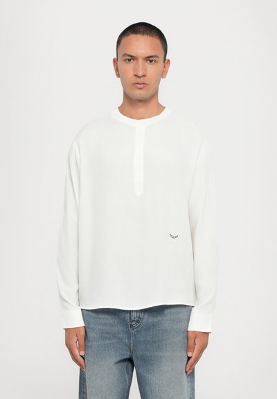 White long-sleeve shirt with a round neckline and a button placket, featuring a small logo on the chest and a relaxed fit.