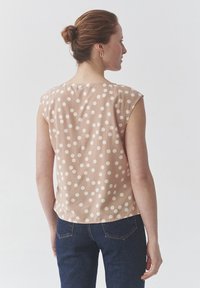Lichtroze mouwloze blouse met grote witte polka dots, ronde halslijn en subtiele drapering. Gestyled met donkerblauwe spijkerbroek.