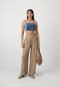 Denim crop top med frynser, beige vide bukser, let strikkede sko og en brun taske. Simpelt, afslappet outfit.