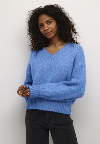 Lichtblauwe gebreide trui met een V-hals, wijde mouwen, geribbelde manchetten en zoom. Gecombineerd met donkergrijze jeans. Zachte en comfortabele textuur.