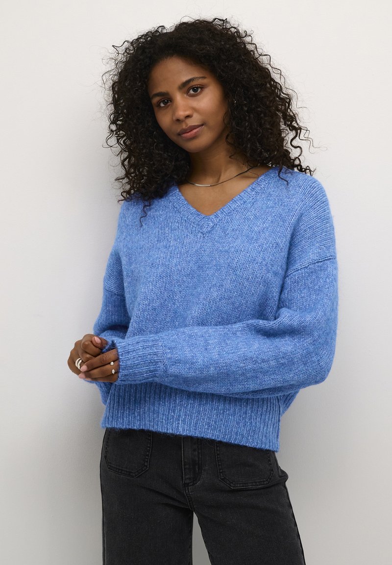 Lichtblauwe gebreide trui met een V-hals, wijde mouwen, geribbelde manchetten en zoom. Gecombineerd met donkergrijze jeans. Zachte en comfortabele textuur.