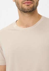 Lys beige kortærmet t-shirt med rund halsudskæring og blød, glat tekstur. Har subtile syninger som detalje.