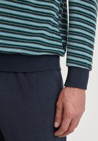Gestreiftes Langarmshirt in Teal, Marineblau und Hellblau mit strukturiertem Stoff und marineblauen gerippten Bündchen. Kombiniert mit dunkelblauen Unterteilen.