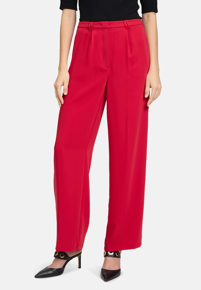 Red wide-leg trousers with pleated front, high waist, and a smooth texture. Paired with black pointed-toe heels featuring gold hardware.
