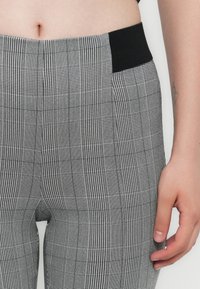 Sive karirane hlače imajo teksturiran vzorec z izmeničnimi kvadrati in črtami, dopolnjuje jih črn elastičen pas.