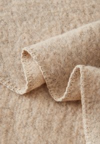 Beige wollen deken met een zachte, gestructureerde oppervlakte en lichtbruine stippen, voorzien van een gestikte rand voor extra detail.