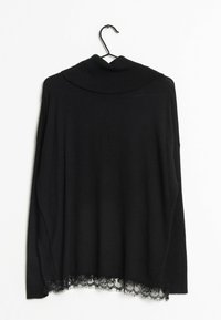 Czarny sweter z długim rękawem i wysokim kołnierzem, z koronkowym wykończeniem u dołu, wiszący na czarnym wieszaku na tle białym.