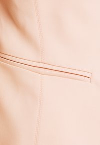 Tissu pêche montrant un gros plan d'une couture et d'une poche zippée avec une texture lisse. Design simple et épuré sans motifs visibles.