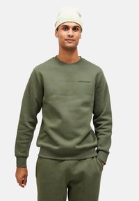 Olijfgroen katoen sweatshirt met geribde boorden en zoom, met een klein Peak Performance-logo op de borst. Draagt met bijpassende broek.