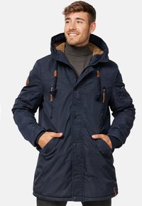 Veste à capuche bleu marine avec une doublure en fourrure texturée, des boutons-pression et des accents en cuir beige ; elle possède deux poches avant et une capuche à cordon.